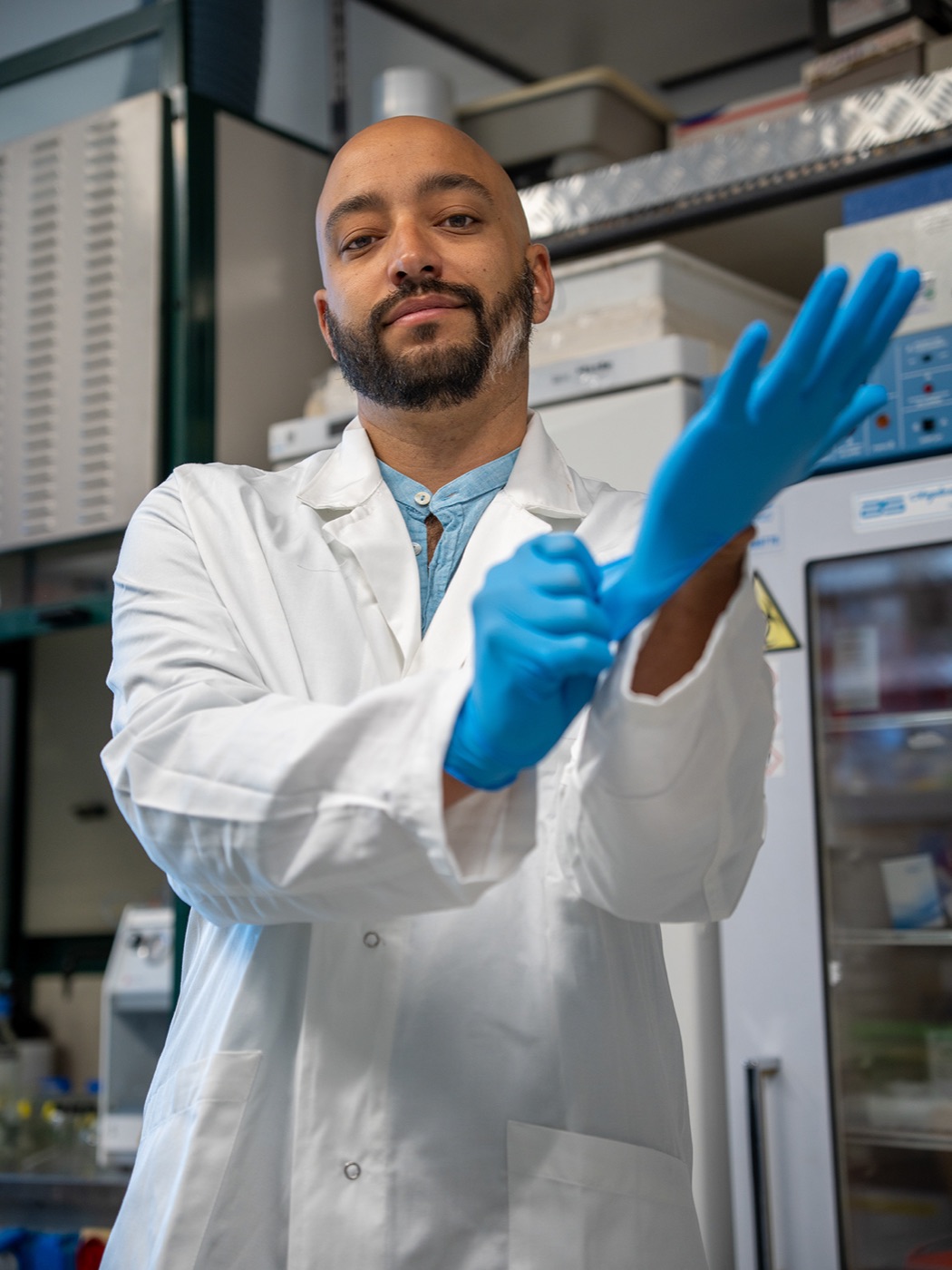 Fred Dante David in a lab coat and blue gloves, working beside laboratory equipment